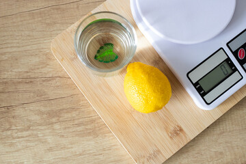 Fresh lemon on a white kitchen scale, a glass of water on the kitchen table. The concept of proper nutrition and healthy lifestyle