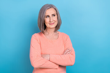 Photo of confident dreamy lady dressed coral shirt looking empty space arms crossed isolated blue color background