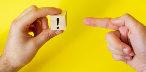 an exclamation mark drawn on a block of wood that a man holds in his hand and the index finger...