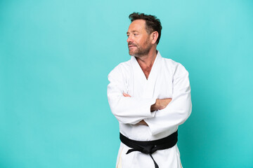 Middle age caucasian man isolated on blue background doing karate keeping the arms crossed