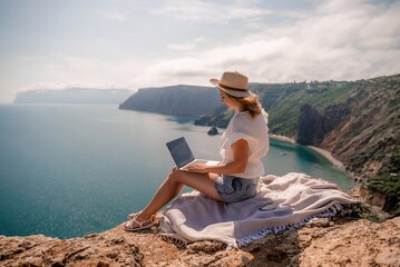 Freelance women sea working on the computer. Good looking middle aged woman typing on a laptop keyboard outdoors with a beautiful sea view. The concept of remote work.