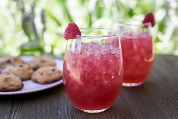 Closeup of red strawberry lemonades with ice put on the table with cookies on blurred background