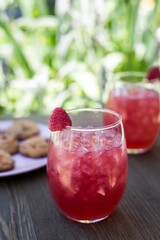 Closeup of red strawberry lemonades with ice put on the table with cookies on blurred background