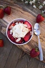 Top view of the fresh and ripe strawberries with white cream in the bowl on the wooden table