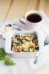Vertical shot of the breakfast casserole in the bowl next to a cup of coffee and slices of butter