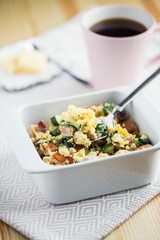 Vertical shot of the breakfast casserole in the bowl next to a cup of coffee and slices of butter