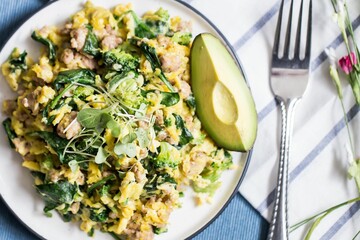 The salad with eggs and avocado on a plate with a fork on a fabric decorated with small flowers