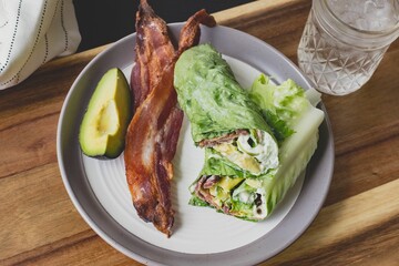 Closeup top view of the lettuce wraps with bacon and avocado on a gray plate with a glass of water