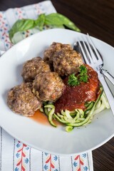 Vertical closeup shot of the meatballs with tomato sauce and zoodles on a white plate