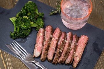 Closeup shot of sliced roasted beef meat with broccoli put on the black board on the table