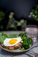 Healthy breakfast with egg, bacon, and lettuce leaves with a glass of water on blurred background