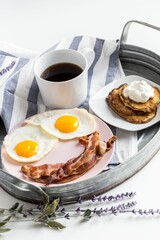 Fresh breakfast with bacons, eggs, a cup of coffee, and pancakes with cream on the tray