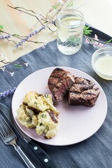 Vertical shot of the steak dinner on a white plate with a sauce and a glass of water on a fabric