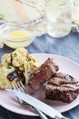 Vertical closeup shot of the steak dinner on a white plate with a sauce and a glass of water
