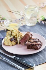 Vertical shot of the steak dinner on a white plate with a sauce and a glass of water on a fabric
