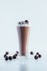 Fototapeta na wymiar Closeup shot of a delicious chocolate shake in a tall glass cup surrounded by cherries