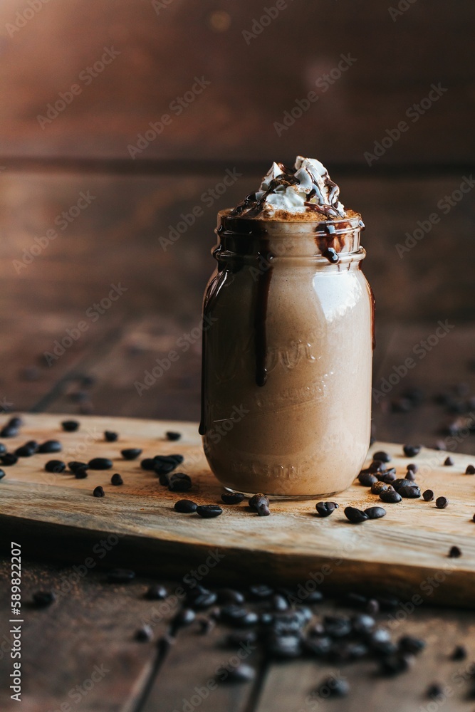 Poster closeup shot of a glass jar of chocolate milkshake topped with whipped cream on a wooden board