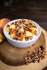 Closeup shot of a bowl of yogurt topped with peaches and walnuts on a wooden board