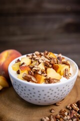 Closeup shot of a bowl of yogurt topped with peaches and walnuts on a wooden board