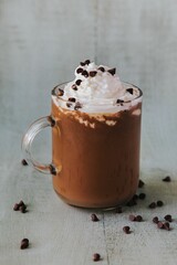 Vertical closeup of a glass of hot chocolate, with cream on top and chocolate pieces on the side