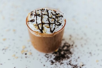 Top view of a glass of hot chocolate on a table, with cream on top and chocolate pieces on the side
