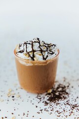 Vertical closeup of a glass of hot chocolate, with cream on top and chocolate pieces on the side