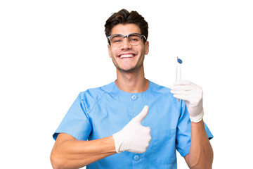 Young dentist man holding tools over isolated background giving a thumbs up gesture