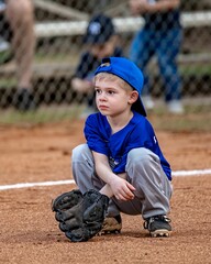 Vertical shot of young adorable baseball player ready to catch the ball with a glove on the field