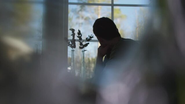 worried man sits by window and runs his hand on face