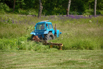 Tractor mowing grass field in the country side. Industrial grass mower work on meadow. Tractor cutting grass in field on sunny summer day. Lawnmover at work in meadow. Agricultural work