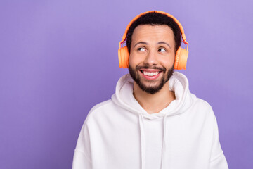 Portrait of minded cheerful person toothy smile look empty space listen music headphones isolated on purple color background