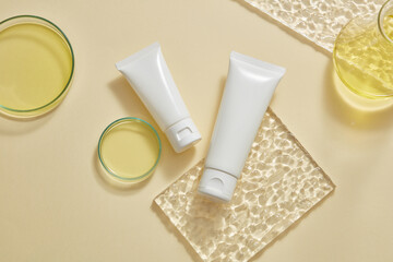 Yellow fluid is contained inside of petri dishes and an erlenmeyer flask, decorated with two unlabeled white tube. Cream, lotion, cleanser product branding mockup