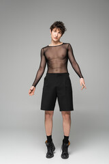 Fototapeta premium full length of nonbinary person in transparent top and black shorts on grey background.