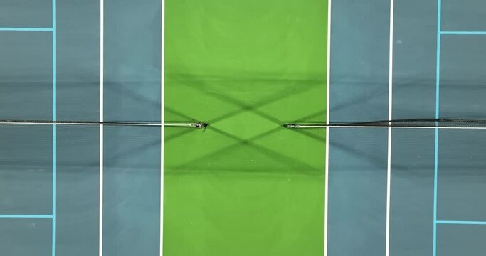 Evening aerial video of outdoor blue tennis courts with pickleball lines with lights turned on.