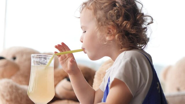 Curly baby girl drinks refreshing lemonade with a straw on a summer day