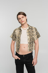 stylish bigender person in snakeskin print blouse posing with hand in pocket of black pants...