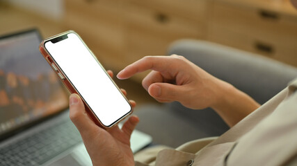 Man sitting on couch at home and using mobile phone. White empty screen for graphic display montage