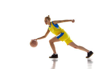 Fototapeta na wymiar Active, athletic, young girl, basketball player in motion, training, dribbling ball against white studio background. Concept of professional sport, hobby, healthy lifestyle, action and motion