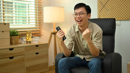 Portrait of excited man with remote controller watching sports match on TV and cheering favorite team