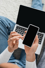 top view of african american student holding smartphone with blank screen near laptop while studying from home.