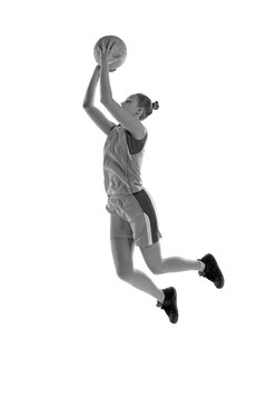 Black and white image of young athletic girl in jump, playing basketball against white studio background. Concept of professional sport, hobby, healthy lifestyle, action and motion