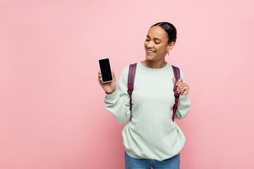 Cheerful african american student looking at cellphone with blank screen isolated on pink.