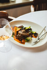 Grilled vegetables in a large white plate. A glass of rose wine on a light background.