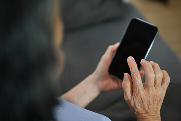 Over shoulder view of senior woman hand holding smart phone, browsing wireless internet or chatting online