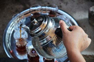 black tea pouring from silver plating teapot with fresh tea leaves, a Glass cup of traditional turkish brewed hot drink