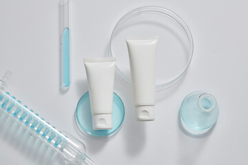 Laboratory concept with test tubes, petri dish and an erlenmeyer flask filled with blue fluid, displayed with empty label tube. Cosmetic packaging mockup