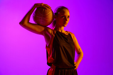 Portrait of young athletic girl, female basketball player in uniform, posing with ball against...