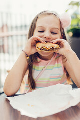 Young girl eating hamburger in fast food restaurant