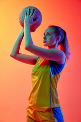 Young concentrated girl, female basketball player in uniform, posing with ball l against white...