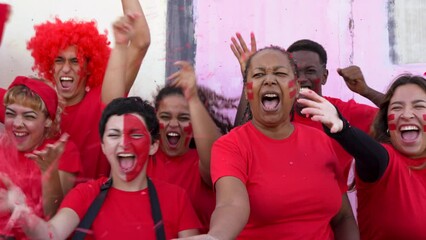 Multiethnic friends football supporter fans watching soccer match at stadium - People with red t-shirts having excited fun on sport world championship event
